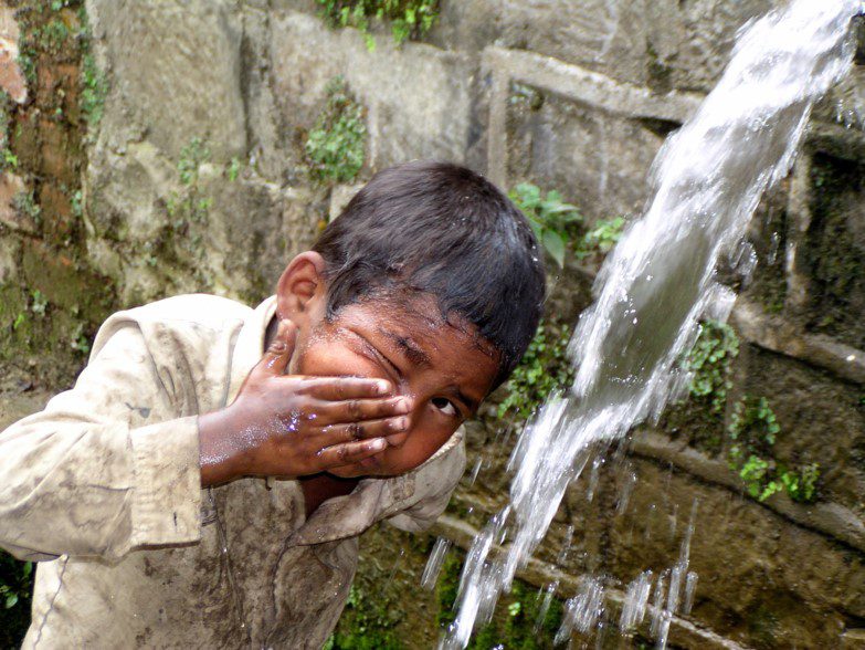 A young boy is washing his face in the water.