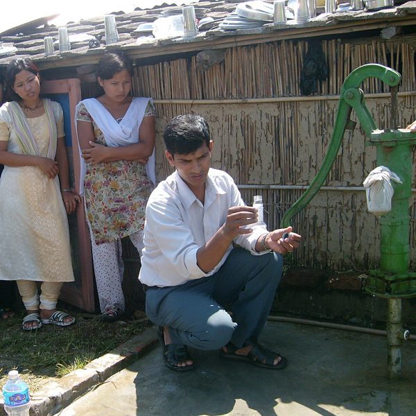 A man is kneeling down next to a green water pump.
