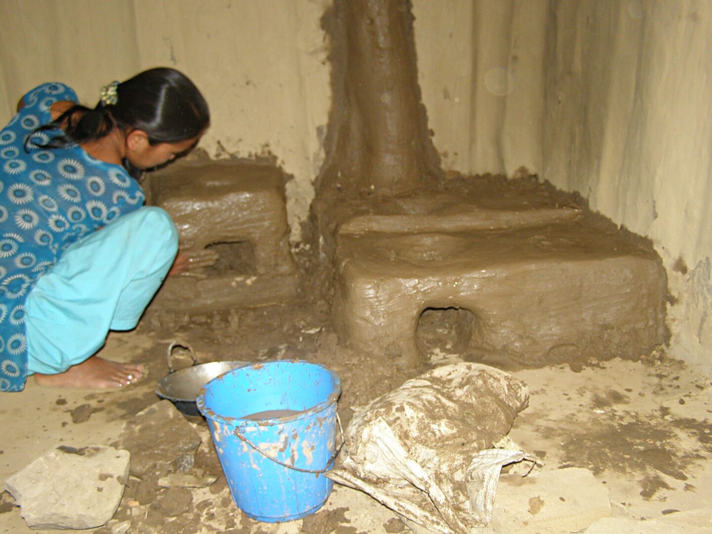 A girl is kneeling down in mud with a bucket.