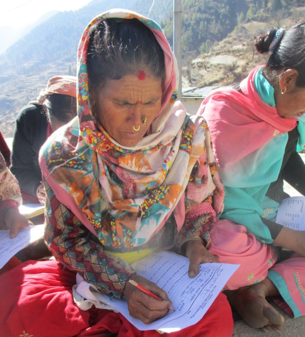 A woman in a colorful dress writing on paper.