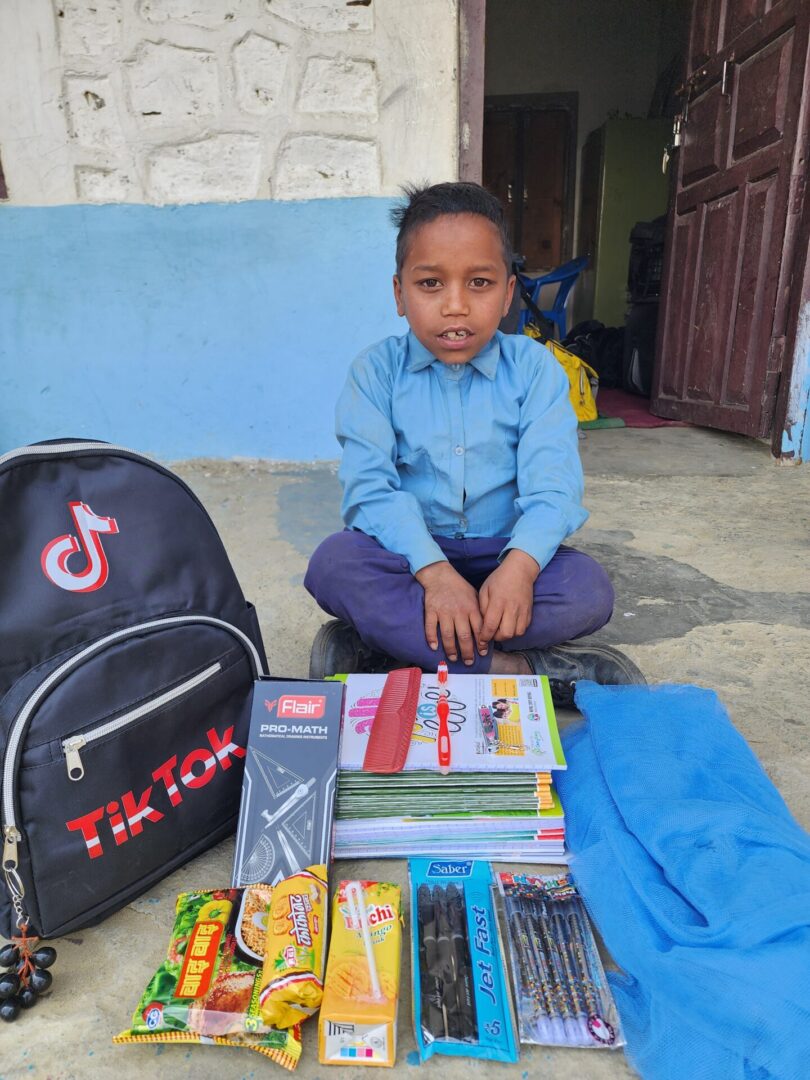 A boy sitting on the ground with his back pack and school supplies.